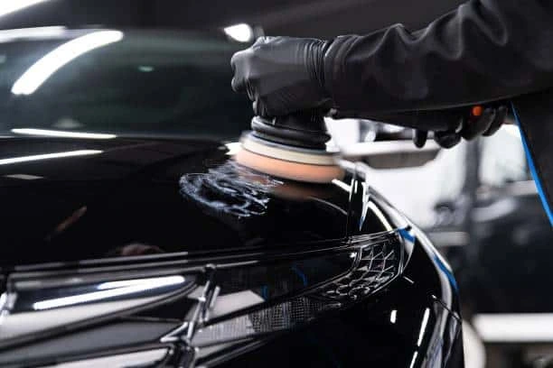 Dual-action polisher buffing a glossy black hood while applying ceramic coating in San Diego