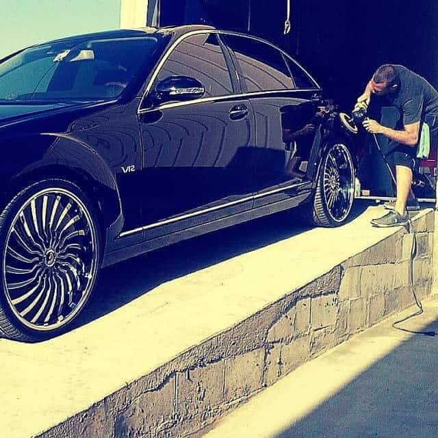 Detailer machine-polishing a black luxury car during paint correction in San Diego