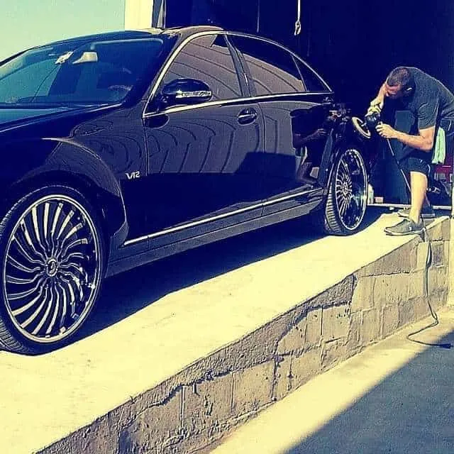 Detailer machine-polishing a dark vehicle during paint correction in San Diego